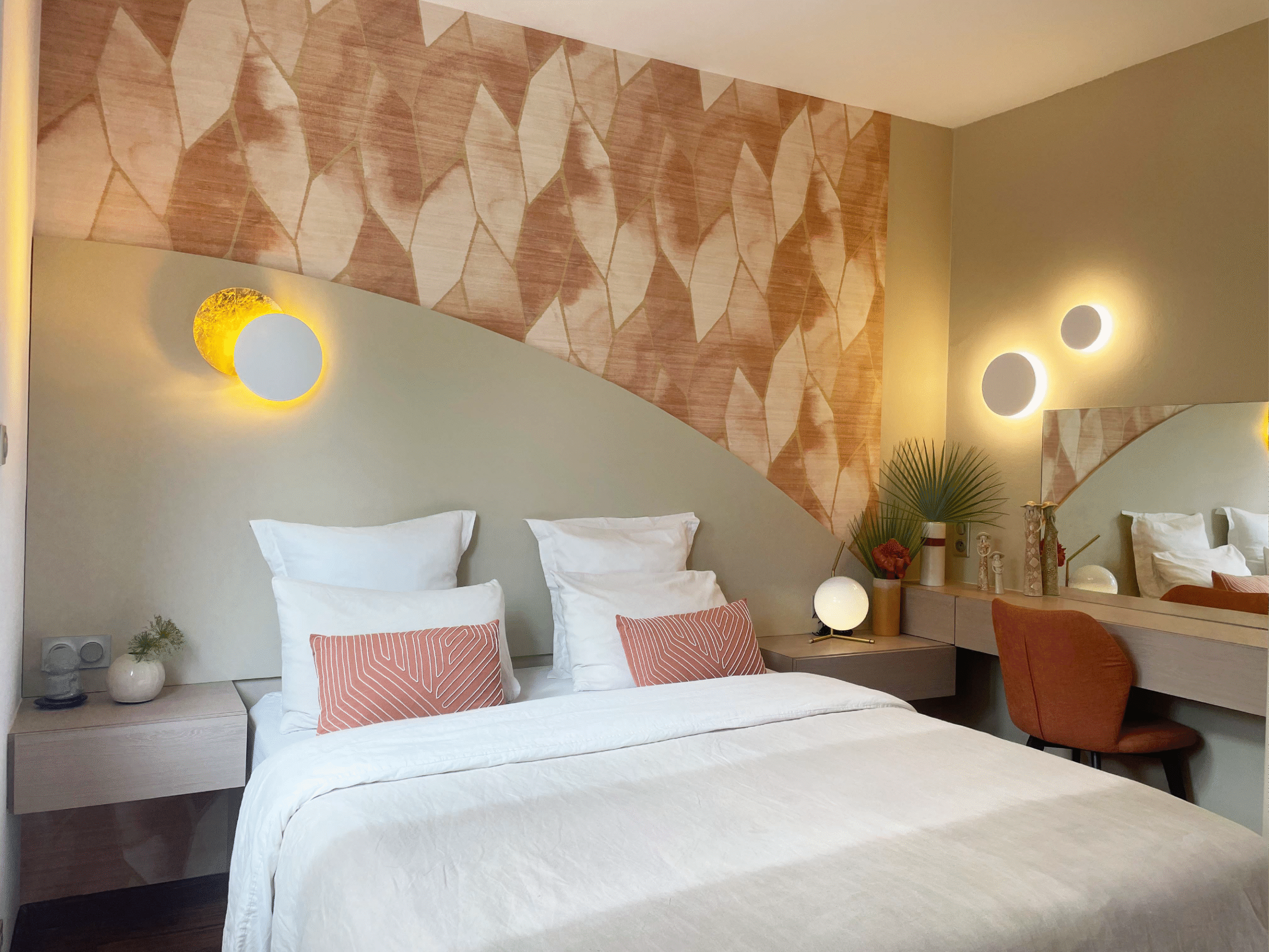 Chambre contemporaine aux tons terracotta et beige, avec tête de lit graphique, éclairages muraux circulaires et bureau intégré, réalisée par Grichka Interiors Design