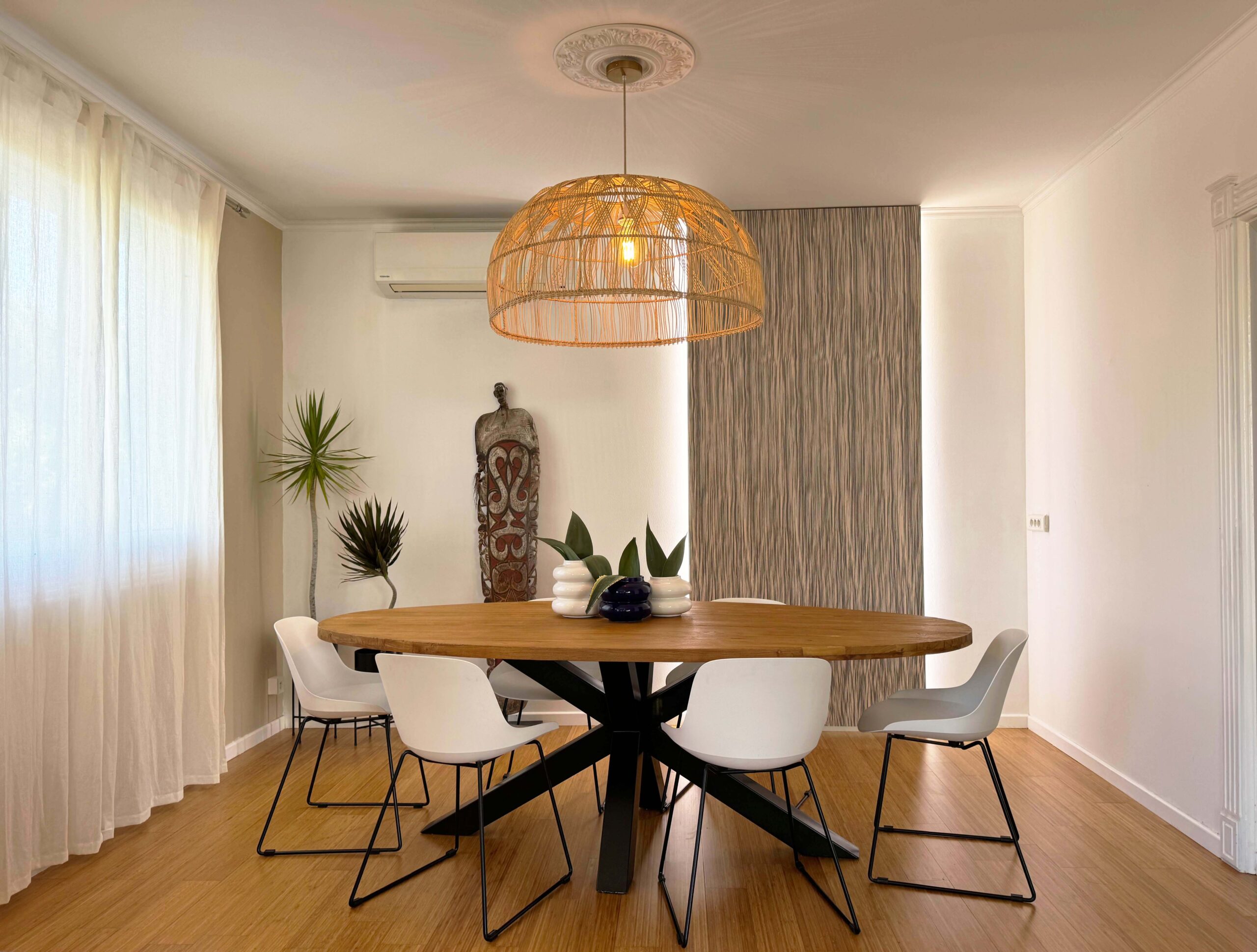 Salle à manger contemporaine avec table ronde en bois, chaises blanches et suspension en rotin tressé, réalisée par Grichka Interiors Design
