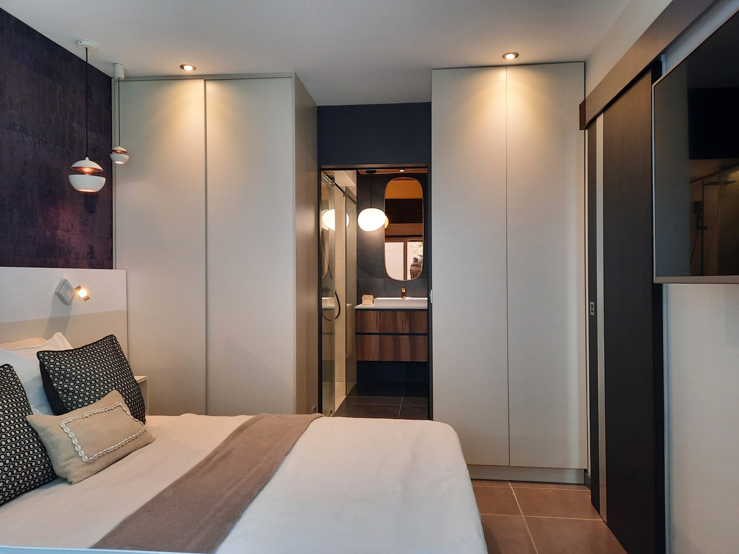 Chambre contemporaine avec éclairage doux, penderies intégrées et salle de bain attenante, réalisée par Grichka Interiors Design