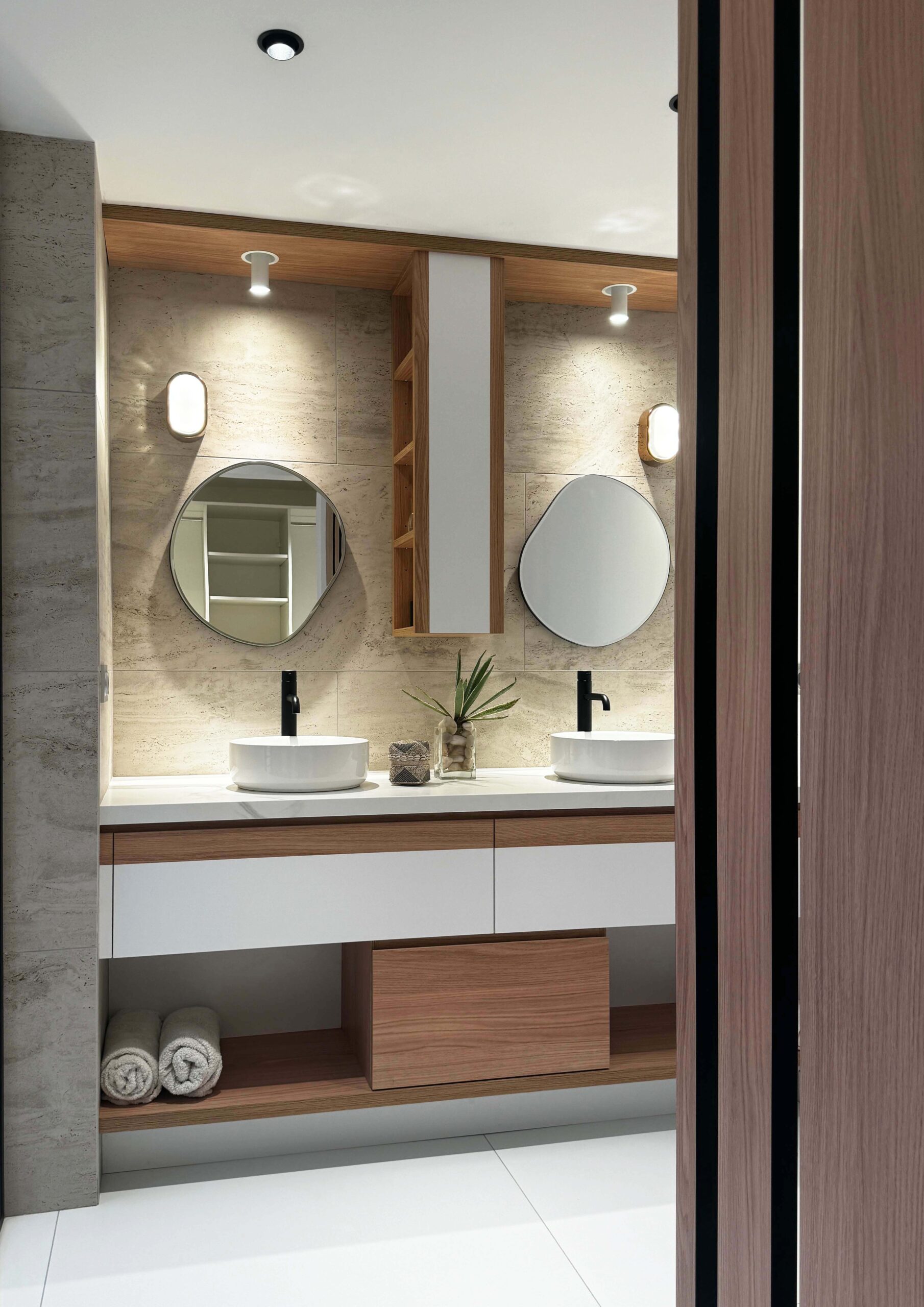 Salle de bain contemporaine avec double vasque, murs effet pierre et mobilier en bois clair, réalisée par Grichka Interiors Design