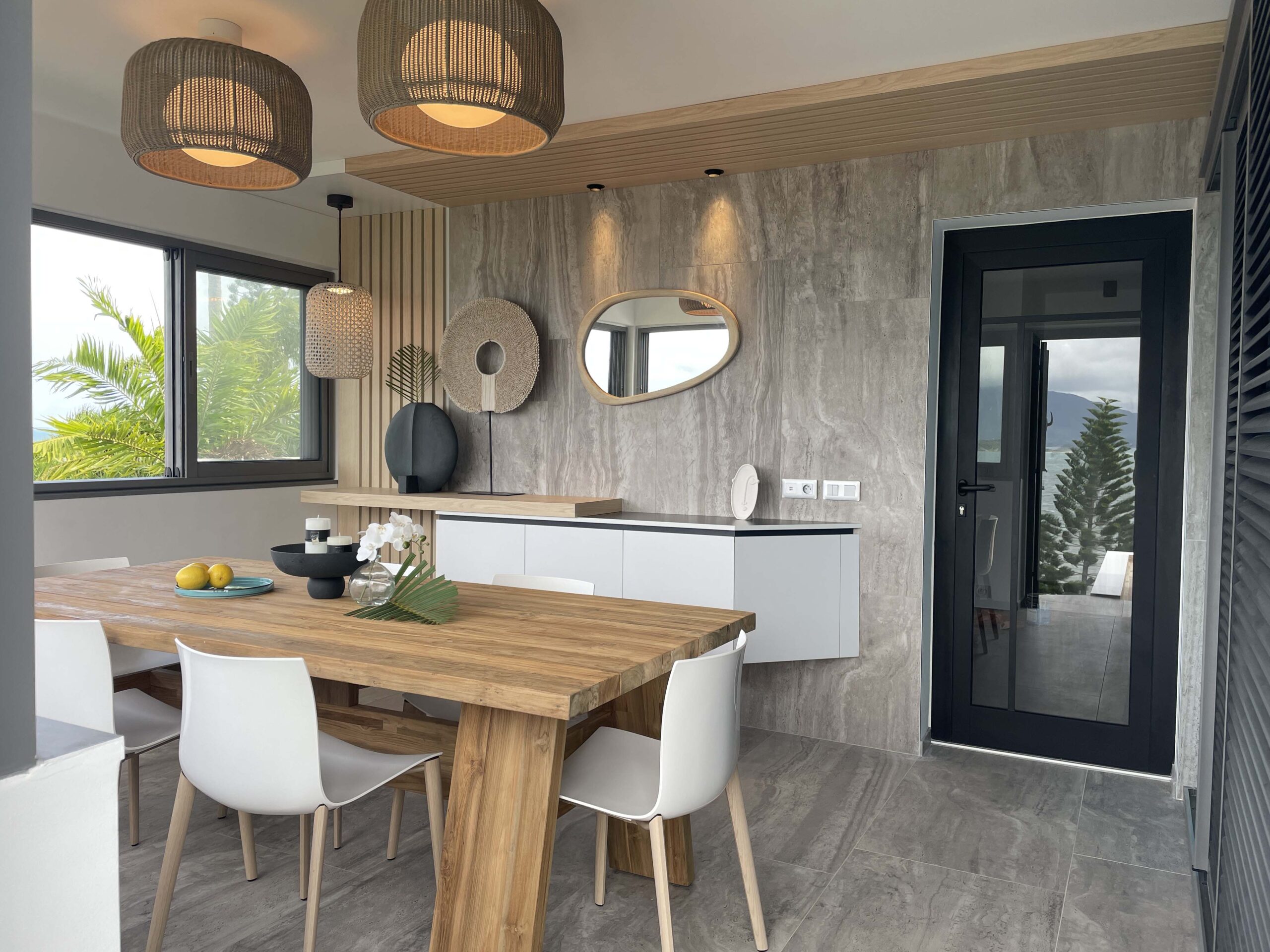 Décoration intérieure naturelle – Grichka Interiors Design Décoration intérieure moderne avec table en bois, objets design noirs, orchidée blanche, mur texturé beige et miroir organique, réalisée par Grichka Interiors Design.