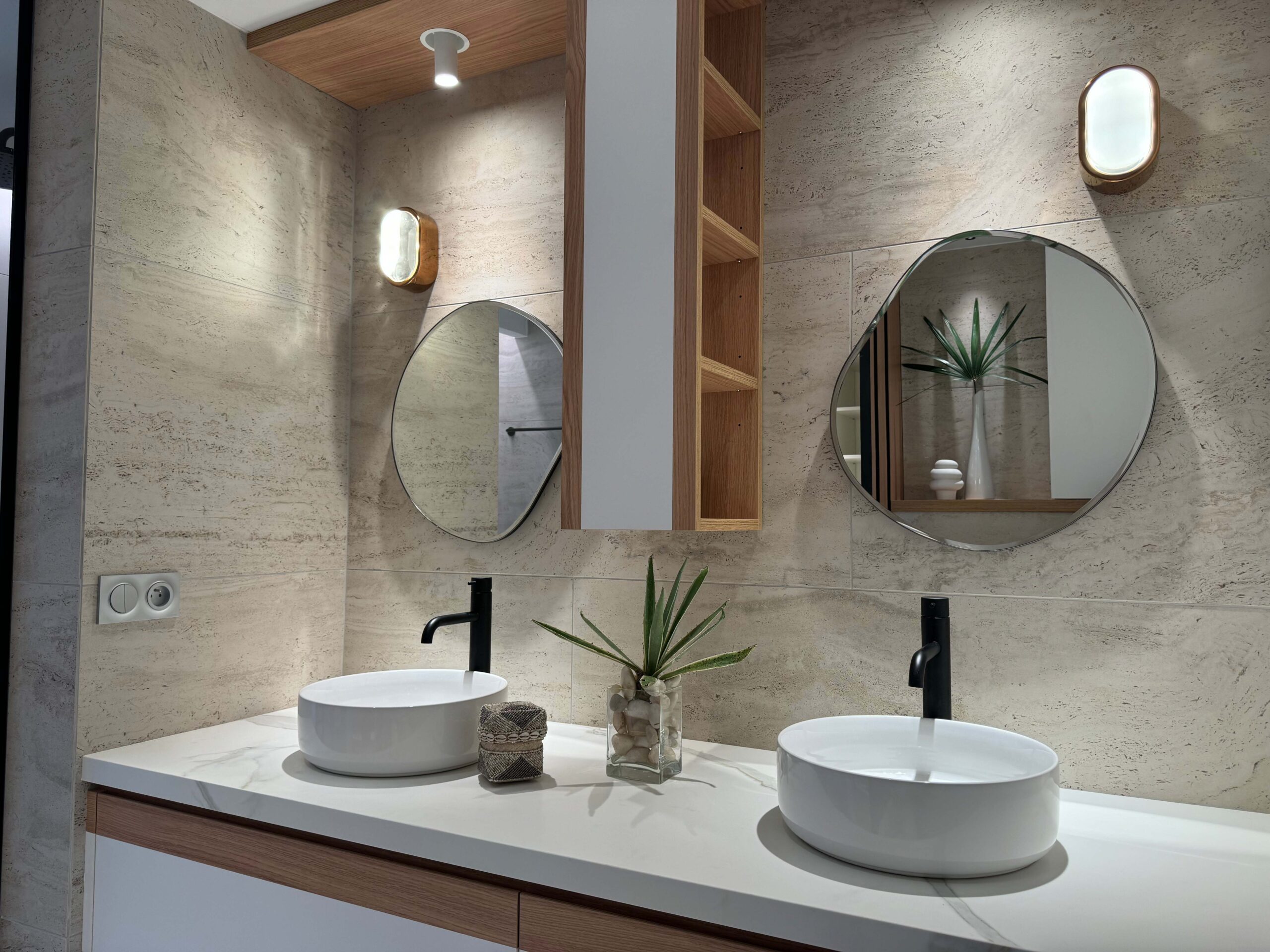 Salle de bain contemporaine avec double vasque sur mesure, meubles en bois et blanc, miroirs aux formes organiques et robinetterie noire mate, réalisée par Grichka Interiors Design.